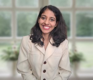 A picture of Madhurya smiling at the camera with a window behind her