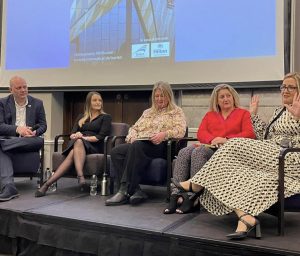 Five people on a stage with one person talking as part of a panel during the conference