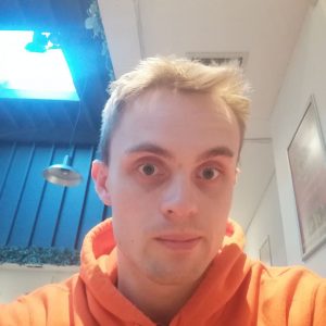 Student Tom poses for a selfie in a bright orange hoodie.
