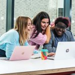 Three students sitting close together looking at a laptop
