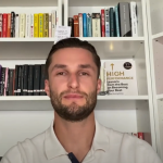 Kristaps smiles at the camera sitting in front of a bookcase