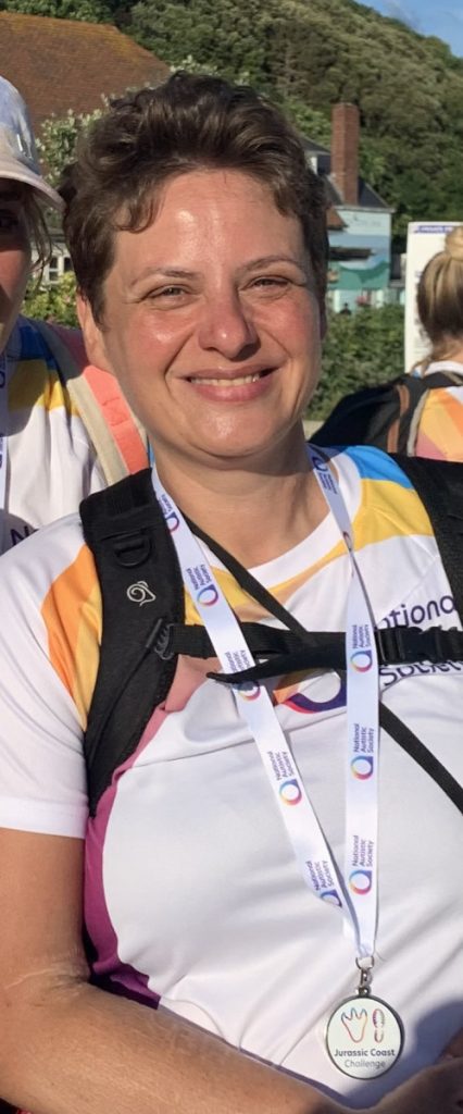 Sarah smiles in a picture she is wearing a medal around her neck and is wearing a backpack 